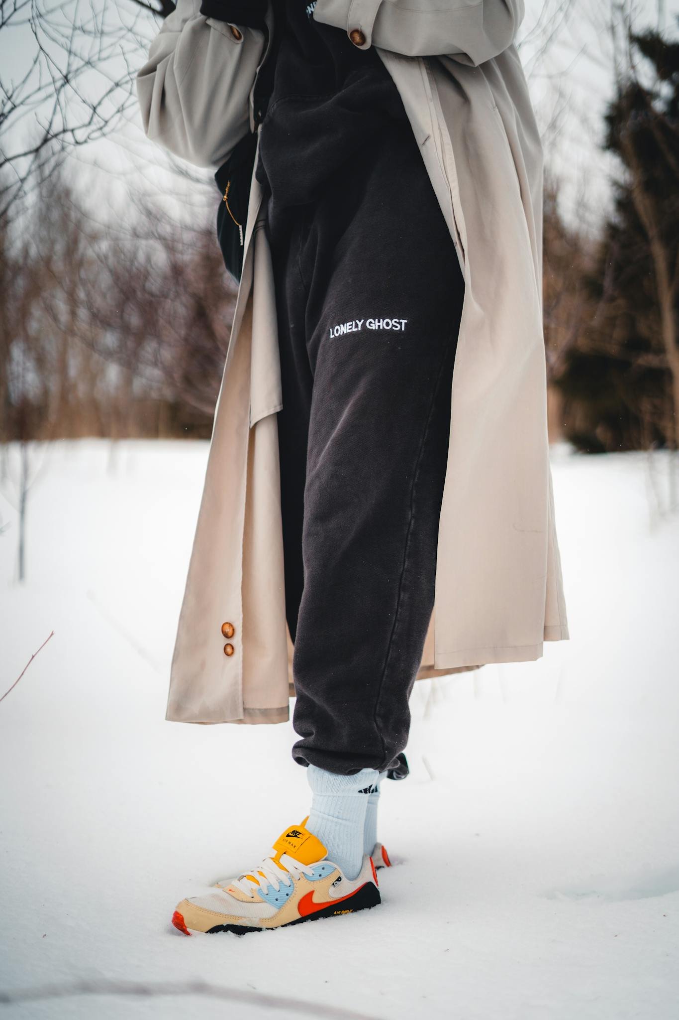 Stylish ensemble featuring a coat and sneakers in a snowy winter setting, highlighting fashion trends.