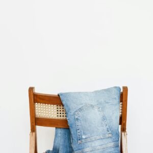 Trendy blue jeans put on back of wooden chair near empty white wall